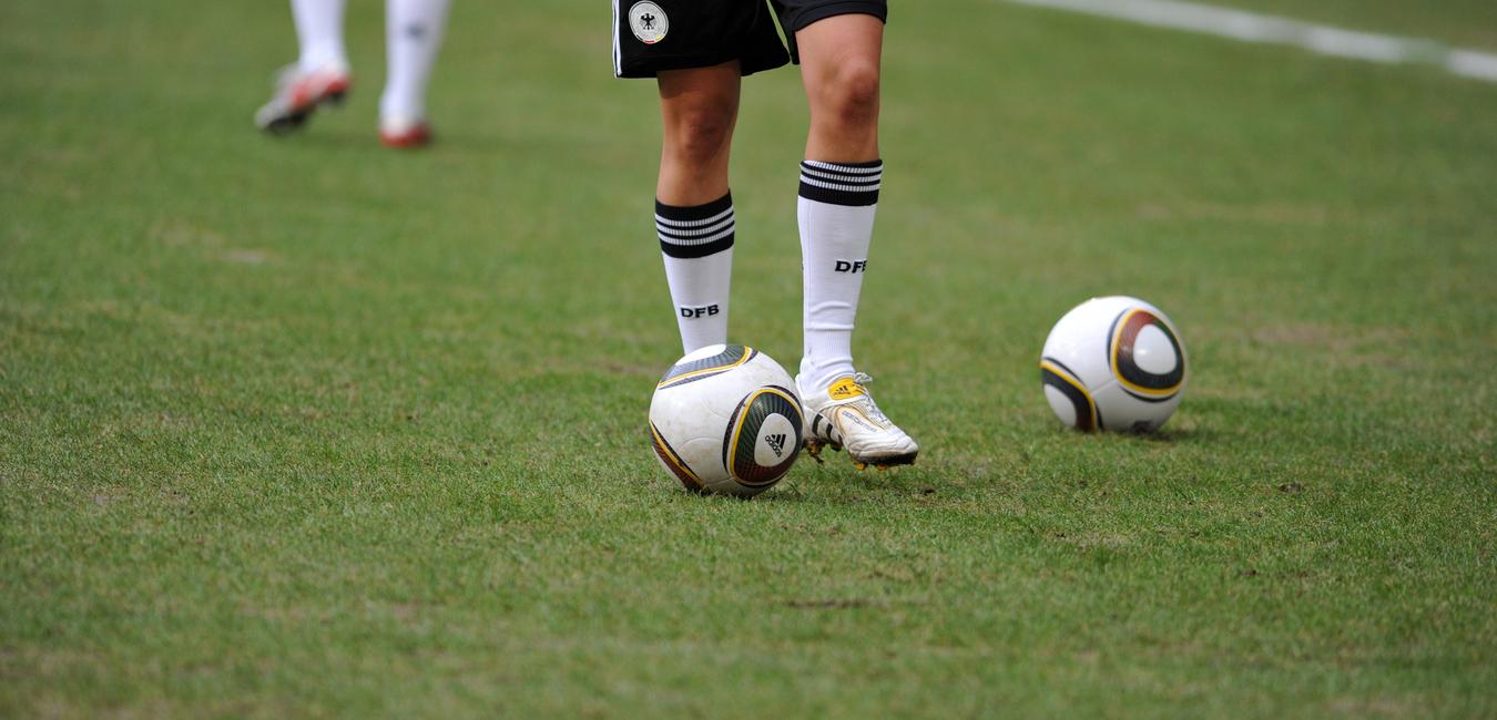 Nahaufnahme eines Fußballspielers mit einem Ball auf dem Rasen, im Hintergrund ein weiterer Ball.