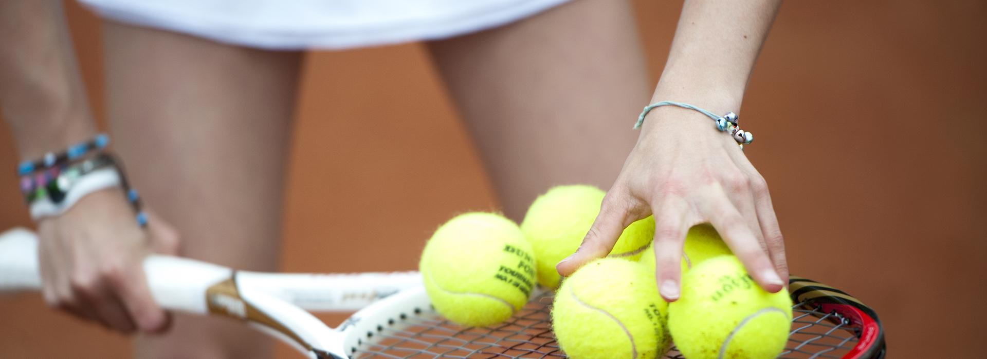 Hand greift mehrere gelbe Tennisbälle auf einem Tennisschläger, während die andere Hand die Schlägerhaltung stabilisiert.