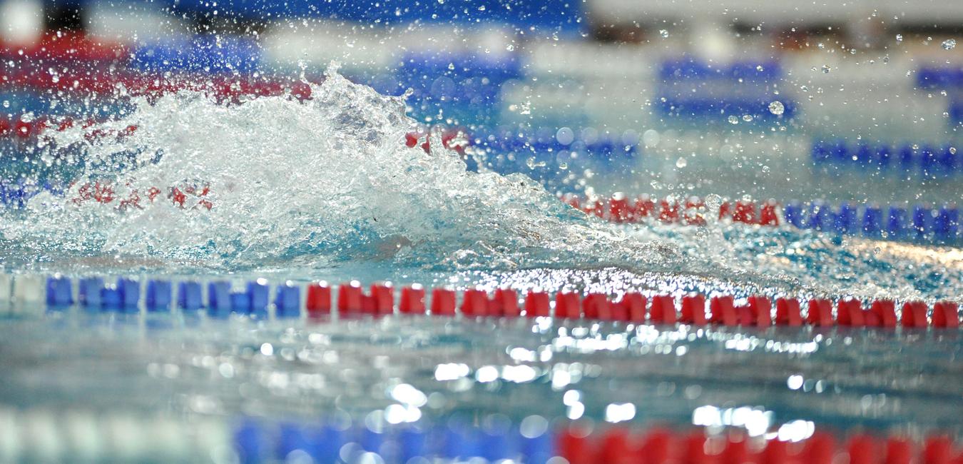 Spritzendes Wasser auf einer Swimmbahn mit roten und blauen Markierungen in einem Schwimmbad.